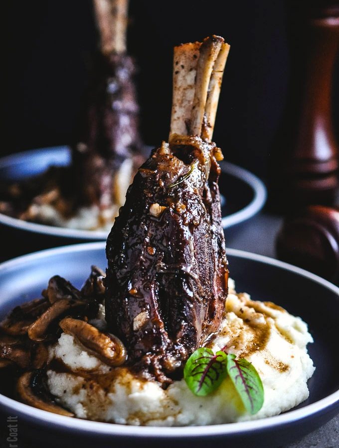 Succulent Sous Vide Licorice Braised Lamb Shanks served on a cloud of mashed potatoes with a side of sautéed flavourful mushrooms.