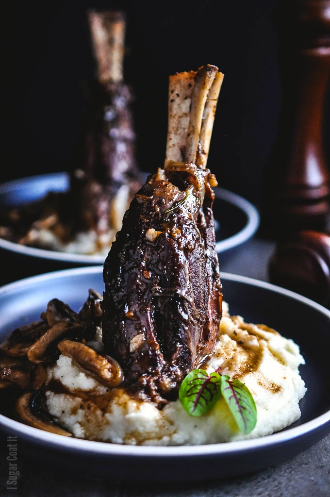 Succulent Sous Vide Licorice Braised Lamb Shanks served on a cloud of mashed potatoes with a side of sautéed flavourful mushrooms.