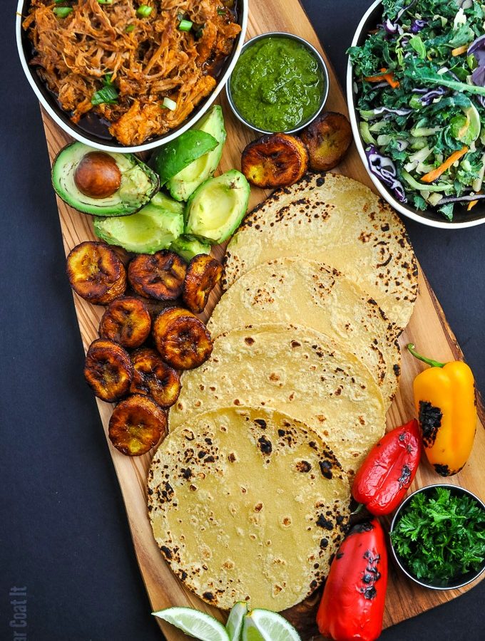 a wooden board with all the fixings for tacos including plantains, avocado grilled vegetables, taco shells and pulled pork | i sugar coat it